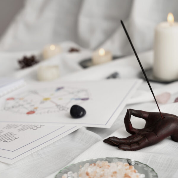 Rituel de purification avec un porte encens en forme de main en position de méditation. Des pierres semi-précieuses sont présentes sur un document de numérologie